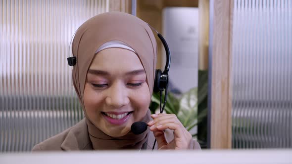 Beautiful woman in hijab at the computer with headset, distant work, call center alt