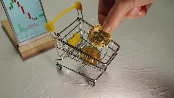 Top view of a man's hand stacking Bitcoin cryptocurrency gold coins in a shopping cart alt