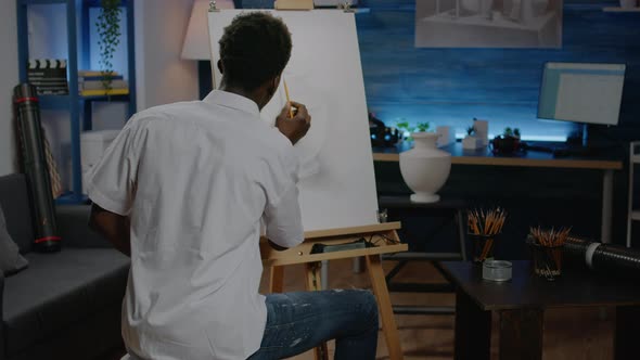 Black Artist Using Pencil on Canvas to Draw Vase alt