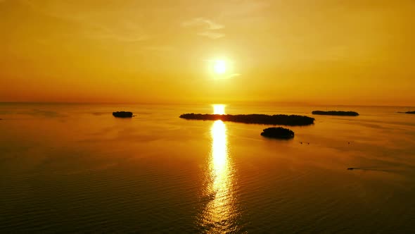 Cinematic aerial view of a dramatic sunset in the ocean with small islands.