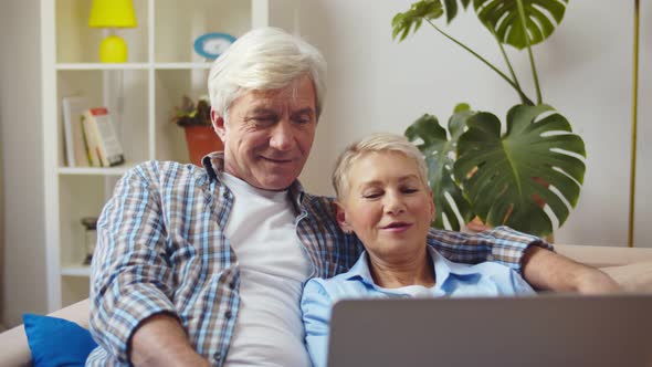 Senior Couple Relaxing and Using Laptop Computer Together Sitting on Sofa in Living Room alt