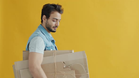 Portrait of Middle Eastern Guy Walking Carrying Cardboard for Recycling on Yellow Background alt