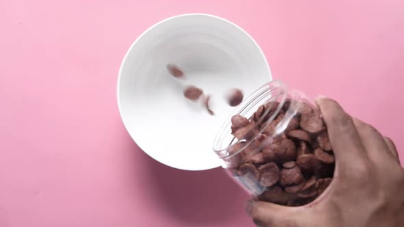Chocolate Corn Flakes Pouring in a Bowl on Pink alt