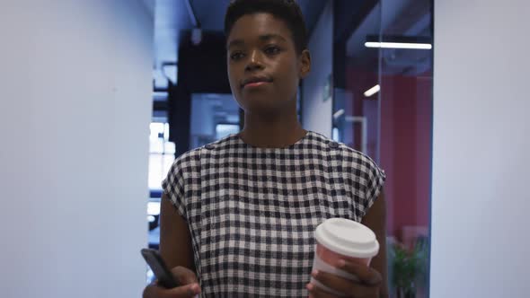 African american businesswoman holding coffee cup walking in office corridor alt