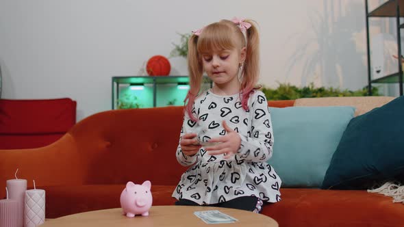 Little Child Kid Girl Putting Money Dollar Banknotes for Future Gift Purchase at Piggybank at Home alt
