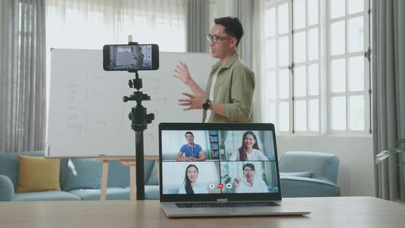 Asian Male Teacher Shoots Video By Smartphone And Having Video Call On Laptop While Teaching English alt