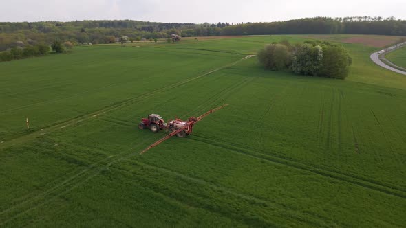 Aerial circular drone footage of a tractor spraying a huge green meadow with water or pesticide with alt