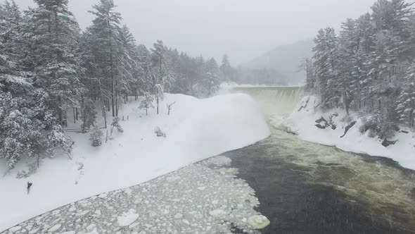 Drone flying thru snowfall towards magical winter scenery of a waterfall alt