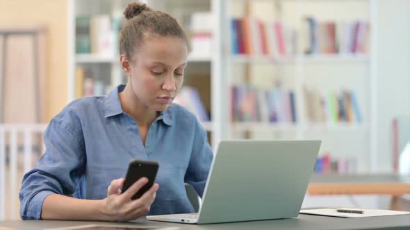 African Woman Using Smartphone and Laptop in Library alt