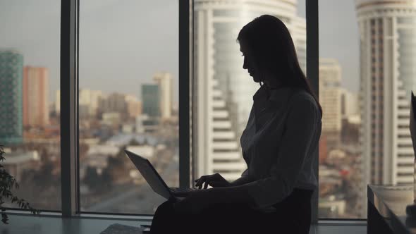Portrait of Business Woman Working on a Laptop By the Window in the Office. Girl Silhouette on a alt