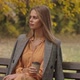 Beautiful Caucasian Woman Sitting on the Bench in the Autumn Park with a Cup of Coffee