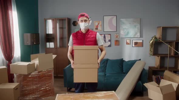 Delivery Man with Covid Mask Holding Carton in New Apartment and Looking at Camera alt