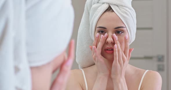 Young Female Stands in Front of the Mirror in Her Bathroom and Applies Cream on Her Face, Skin Care alt