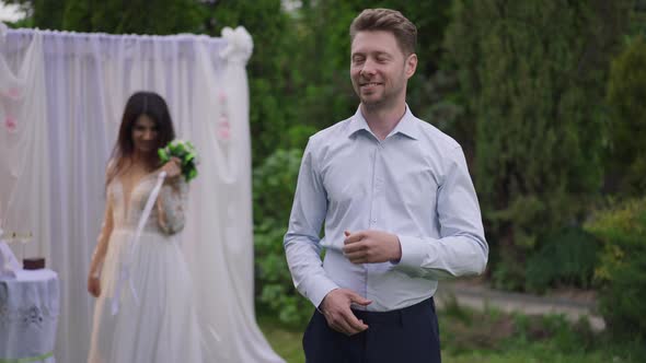 Confident Proud Caucasian Man Posing on Marriage Ceremony Looking Back at Happy Middle Eastern Woman alt