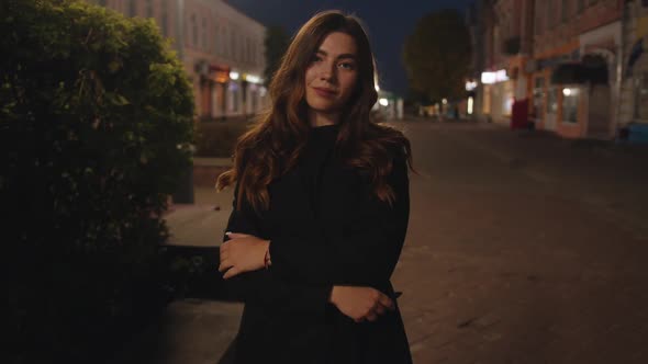 A Glamorous Young Girl Stands with Her Arms Crossed on Her Chest on a City Pedestrian Street in the alt