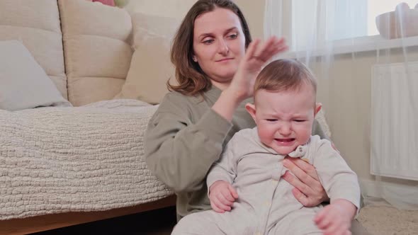 The mother pities the crying baby and strokes his head with her hand, age 8 months