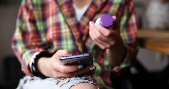 Woman holding in hand a bottle of pills and checks pills medicines using her smartphone alt