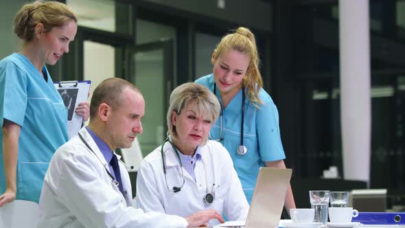 Doctors and nurse discussing over laptop in conference room alt