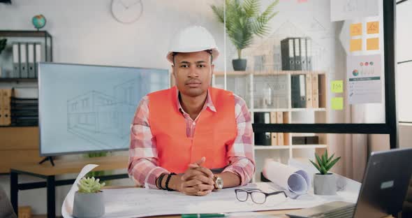 Architect in Vest and Hardhat Posing on Camera at his Workplace in Modern Design Office alt