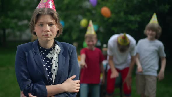 Sad Bullied Teenage Girl with Crossed Hands Standing in Spring Summer Park with Blurred Friends alt