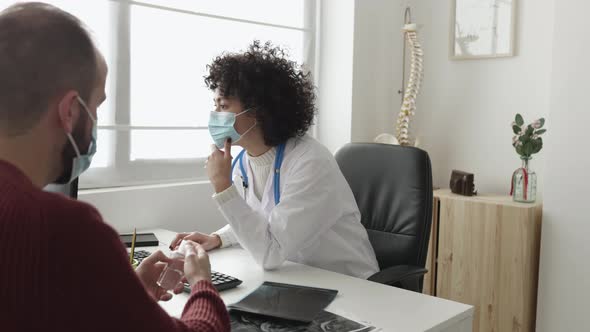 Doctor and Patient in Face Mask Talking in a Medical Consultation in a Clinic alt