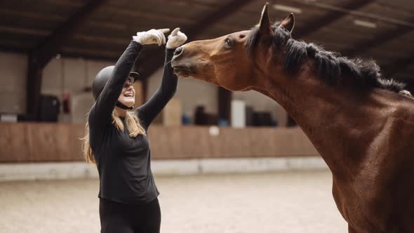 Woman In Riding Hat Pointing Upwards To Horse In Paddock alt