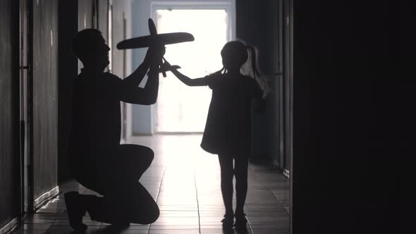 Silhouettes of Dad and Little Daughter Playing with Airplane Toy