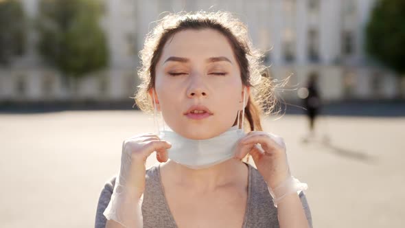 Happy Hispanic Girl Walking Outdoor While Taking Off Her Protective Face Mask and Looking at Camera alt