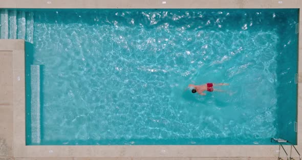 View From the Top As a Man in Red Shorts Swims in the Pool alt