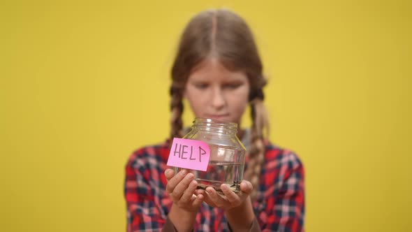 Help on Aquarium Bottle with Little Fish in Hands of Blurred Teenage Girl at Yellow Background alt