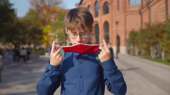 Portrait of Teenage Student Putting on Safety Mask Standing Outdoors alt