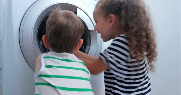 Cute Children Looks Inside the Washing Machine. Cylinder Spinning Machine. Concept Laundry Washing alt