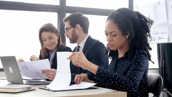 Young Pretty Positive African American Business Woman Sitting at the Workplace in Modern Office alt