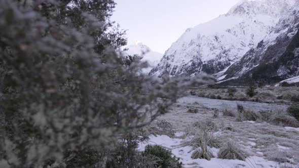 Reveal shot of running river in a valley surrounded by snow capped peaks and mountains in winter, Ne alt