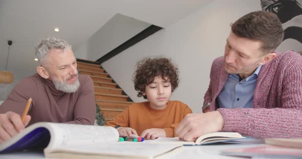Gay Parents Help Little Son with Homework Sitting at Desk alt