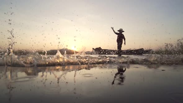 Silhouette fisherman throwing fishing net during sunset with boats at the lake.