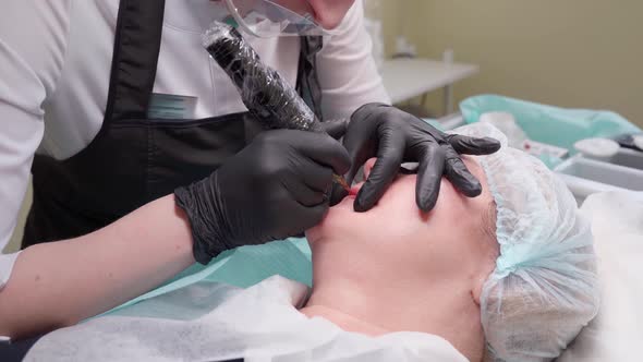 Hand Makes Permanent Makeup Lips Procedure Applying Pigment Makeup on Lips with Tattoo Machine alt