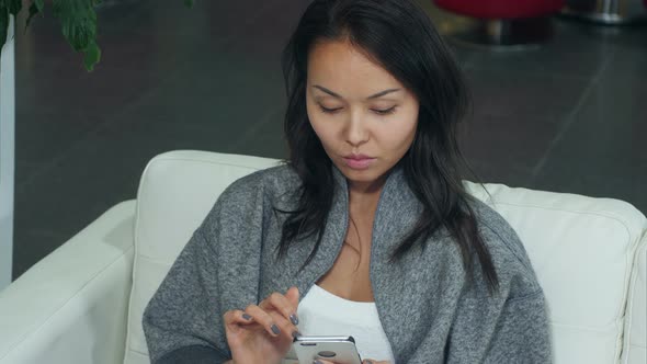 Cute Asian Woman Relaxing on Sofa and Using Smartphone alt