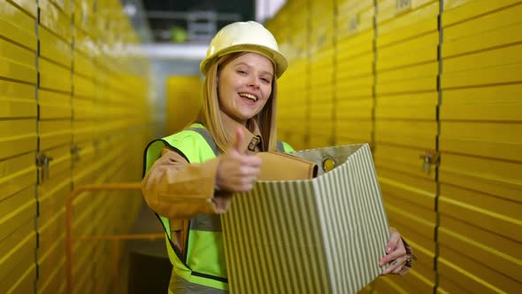 Medium Shot of Happy Young Woman Posing with Box Gesturing Thumb Up Smiling Looking at Camera alt