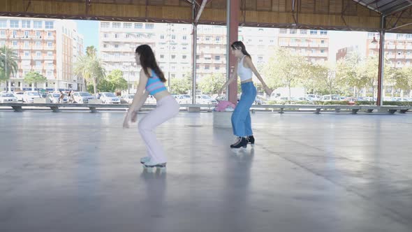 Three Darkhaired Girls Do Tricks on Rollerskates Following Side View alt