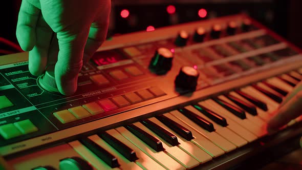 slow motion shot of a man playing keys and turning knobs on a vintage synth, red and green mood alt