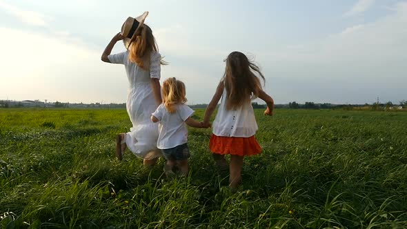 Young mother walks and runs with her little girls, children, on green grass.