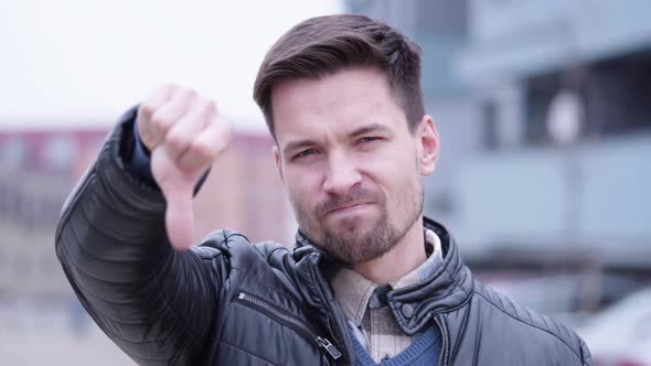 A Young Handsome Man Shakes His Head and Shows a Thumb Down To the Camera in a Suburban Area alt