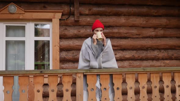 Woman in a Knitted Red Hat and Scarf Drinks Hot Tea Standing alt