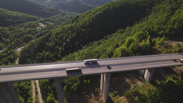 Aerial View of White Cargo Semi Truck Driving on Two Way Motorway Viaduct Over Green Hills alt