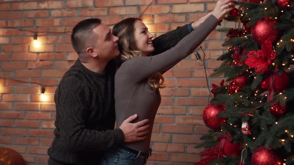 Young Couple Decorating Christmas Tree Together at Home alt