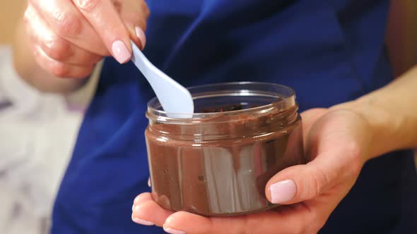 Beautician Takes Chocolate Cream for Beauty Procedure From Jar with Spatula alt