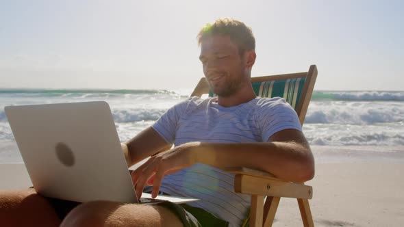 Man using laptop at beach in the sunshine 