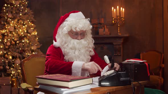 Workplace of Santa Claus. Cheerful Santa is working while sitting at the table. alt