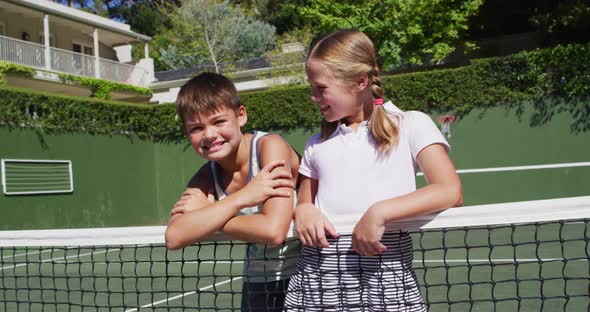 Portrait of caucasian brother and sister smiling together while standing at at tennis court on alt